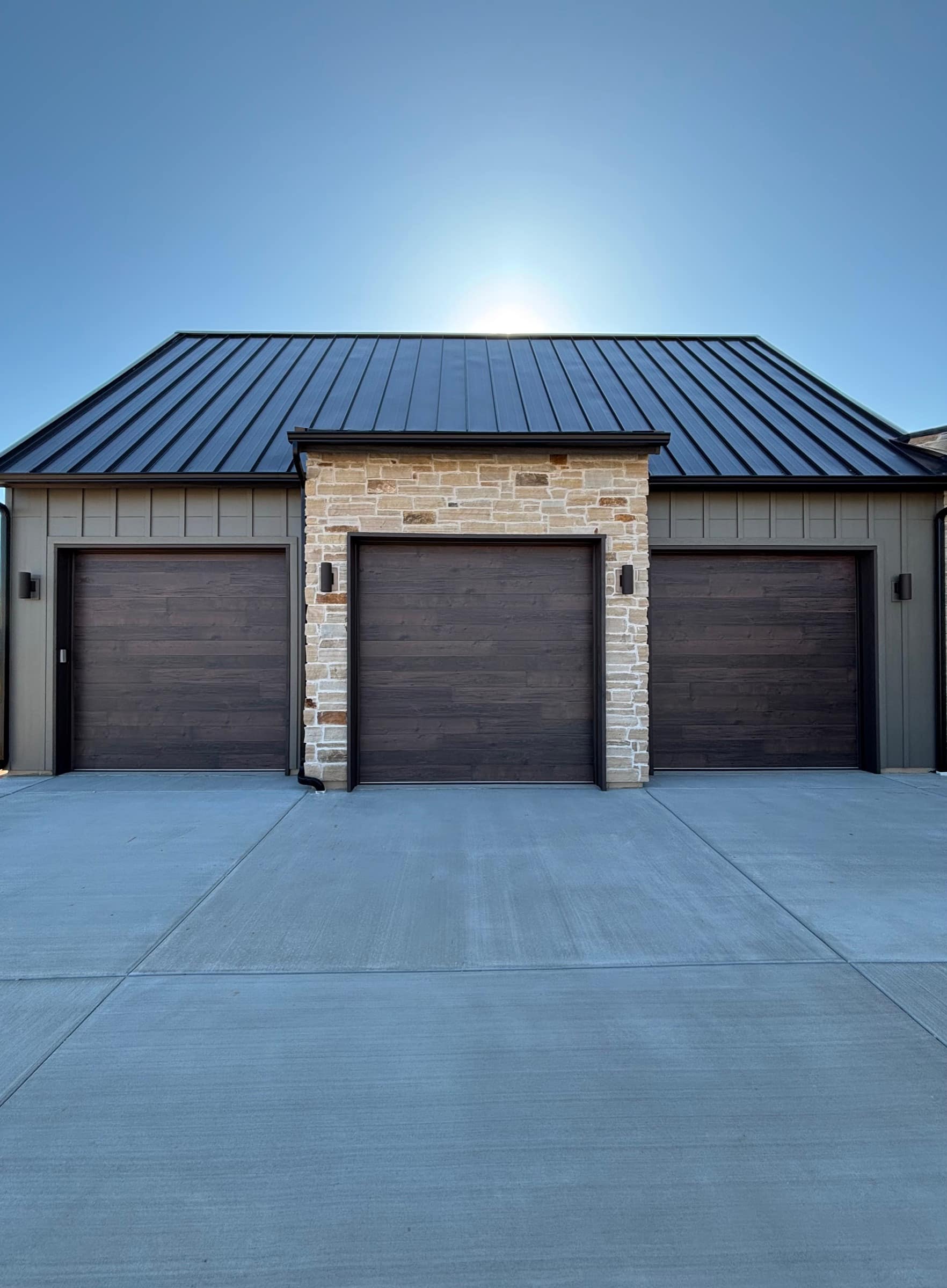 A kraftsman-built Kooler garage door on a stone-pillar home facade in summer light