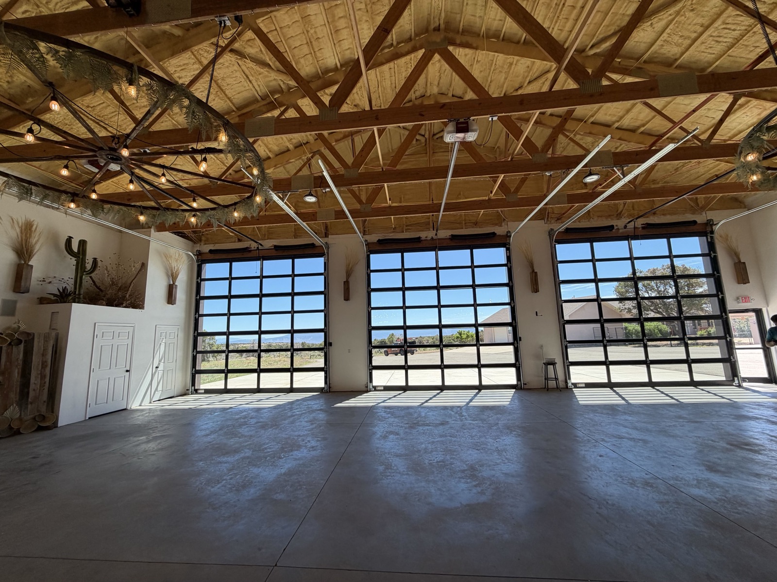 Commercial event space with three full-view aluminum and glass Kooler garage doors, wood-truss ceiling, and warm string lighting