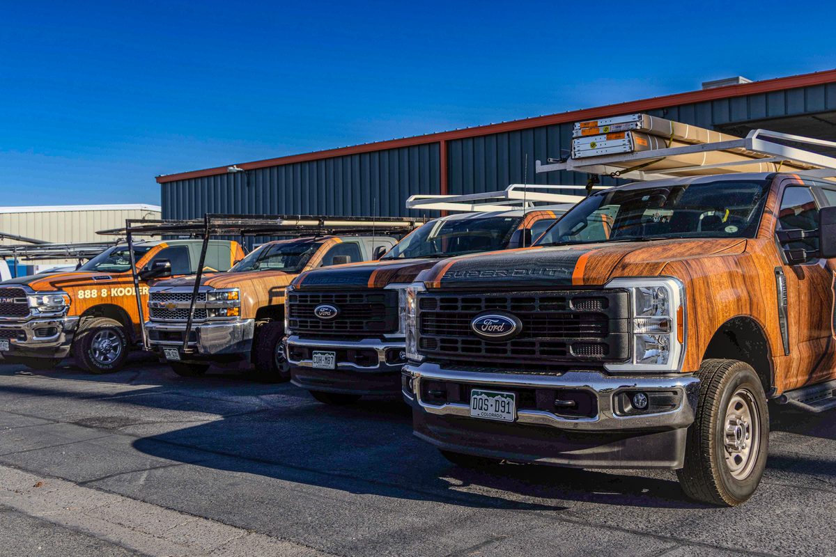 Four wrapped Kooler Garage Doors service trucks lined up at the shop under a clear sky.