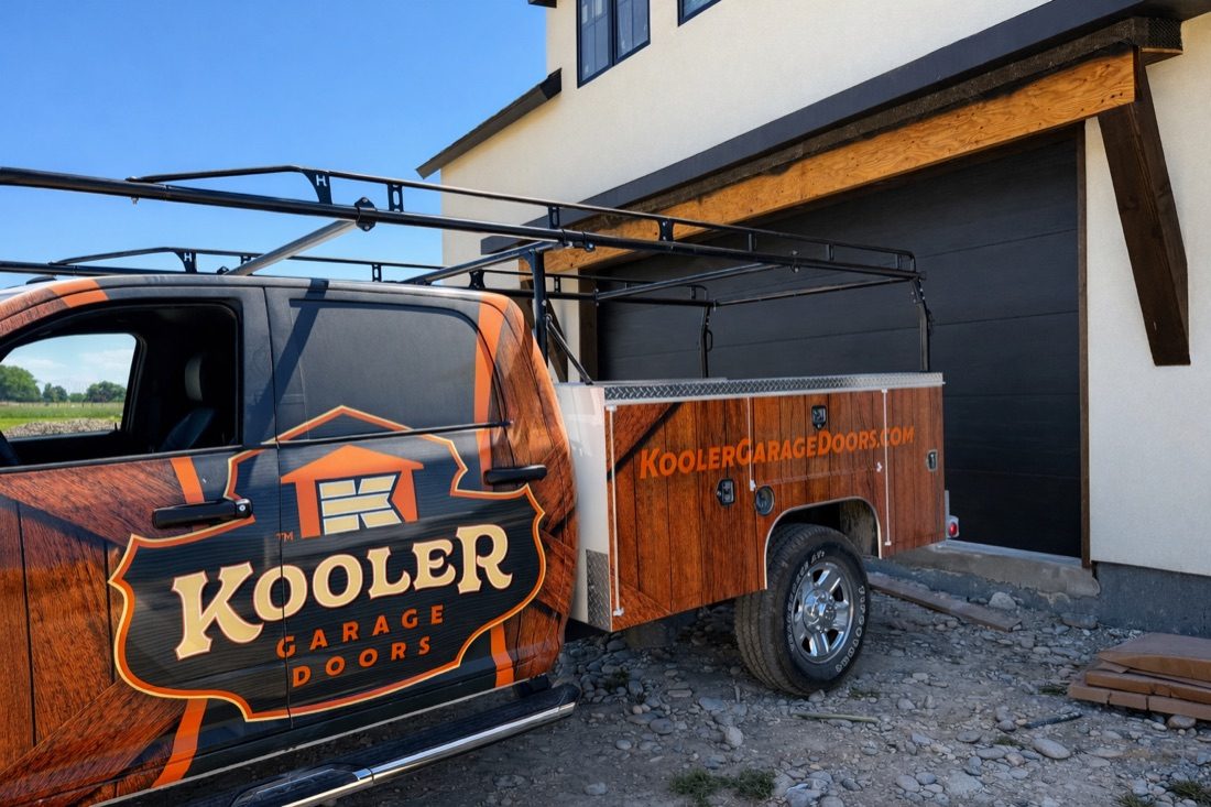 A Kooler Garage Doors service truck parked at a new-construction home, the new dark garage door already hung behind it.
