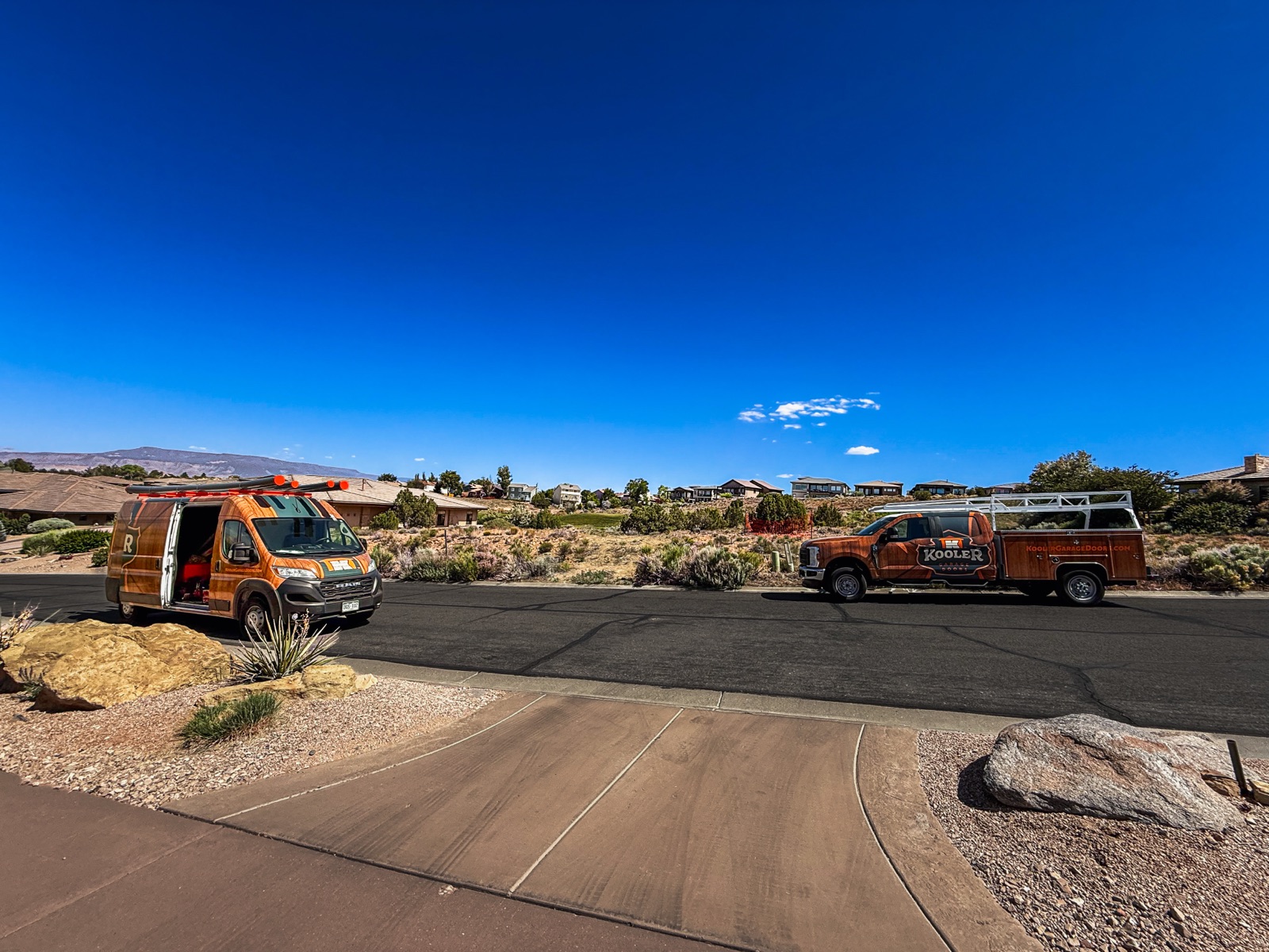 Two wood-wrapped Kooler Garage Doors trucks on a Western Colorado street under a clear blue sky