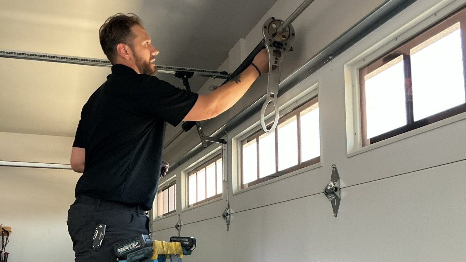 A Kooler Garage Doors Kraftsman on a ladder inside a customer's garage, adjusting the hardware on the door with a wrench