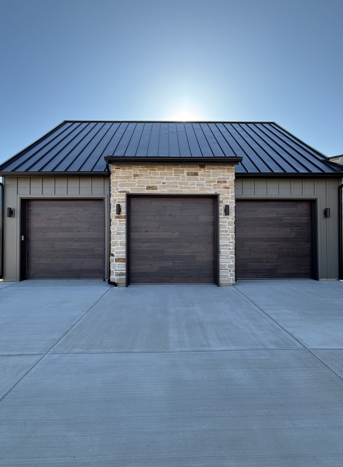 Modern wood-grain garage doors framed by stone columns under a black standing-seam roof