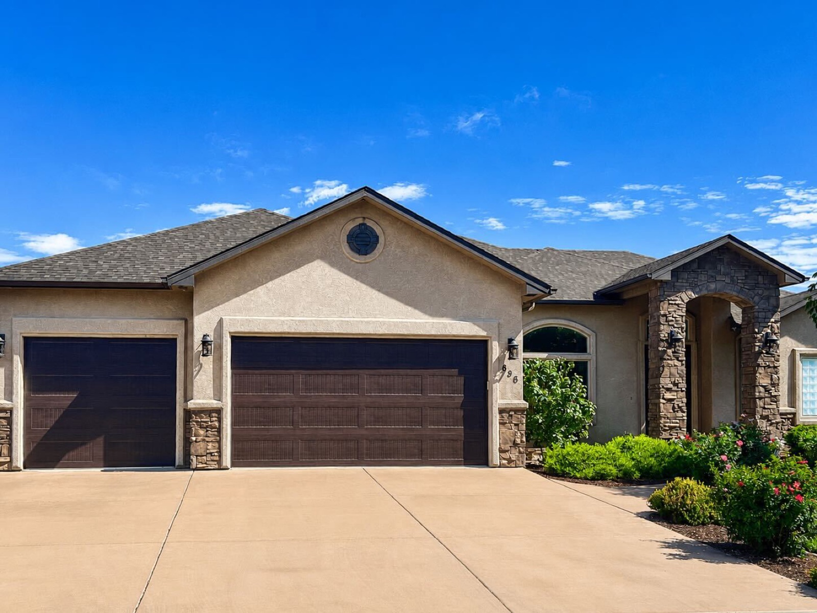 Stucco-and-stone ranch home with dark raised-panel garage doors