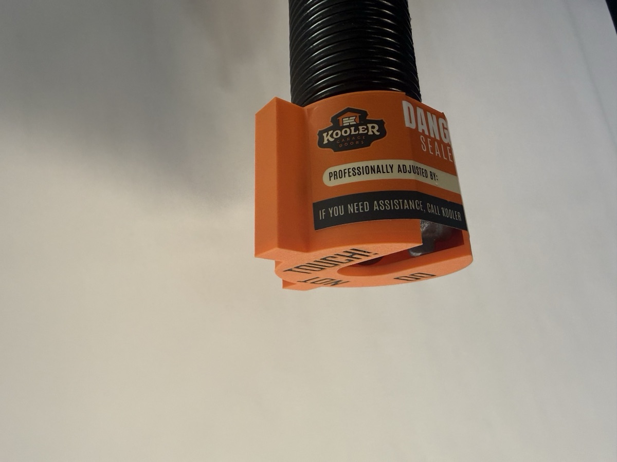 K Kap detail — 'Do Not Touch!' warning embossed on the cap face, covering the adjustable winding-cone end of a torsion spring where 250-400 ft-lbs of torque is stored.