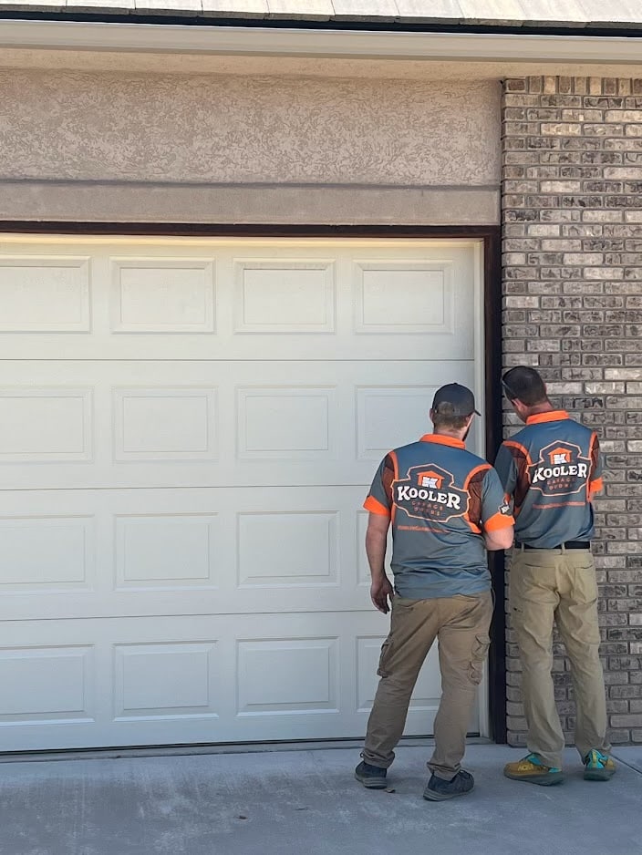 Two Kooler Kraftsmen in branded jerseys inspecting a residential garage door before running the Door Score on the Western Slope