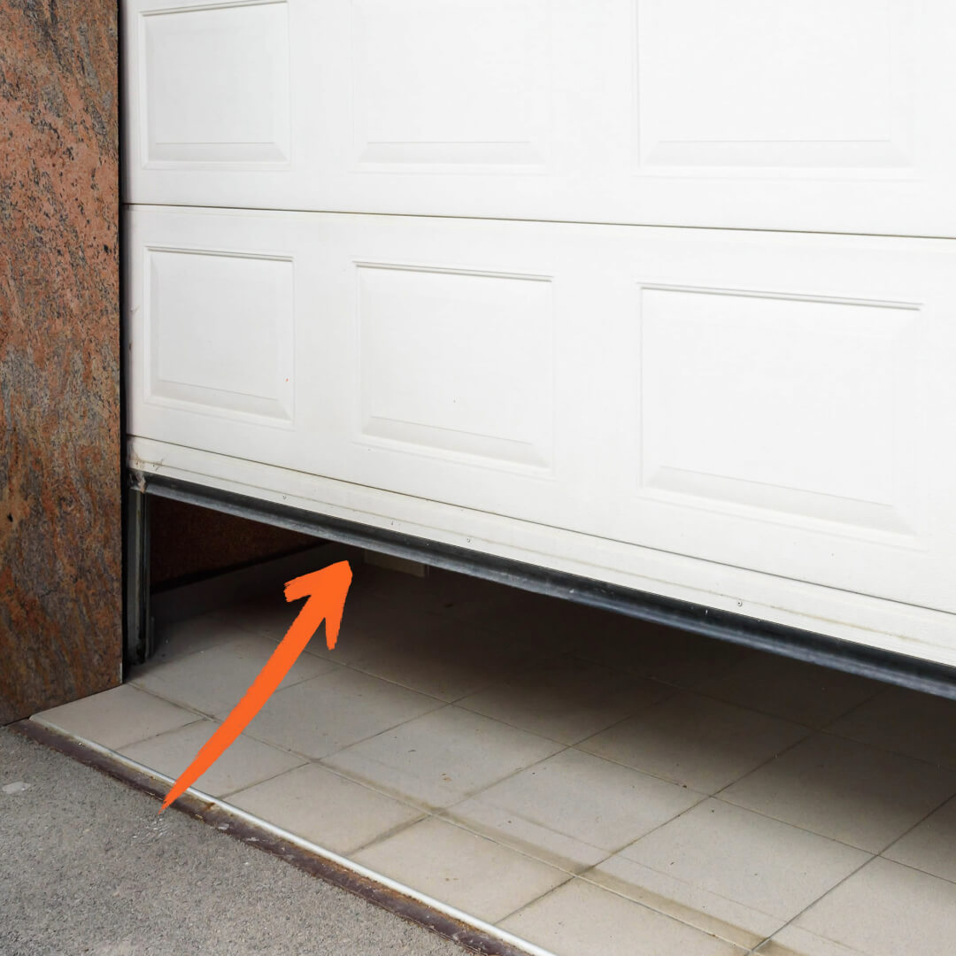 image of slightly open garage door with an arrow pointing at garage door weather stripping replacement piece